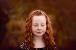 Portrait showing bright red curly hair against dark background.