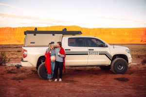 Couple poses beside lifted white pickup truck in desert landscape.
