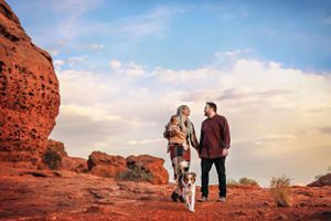 A couple and their dog explore red rock formations in a desert landscape at sunset.