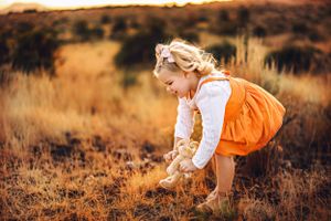 A child in orange overalls bends down to explore in a golden autumn field near Pine Valley Utah, Southern Utah
