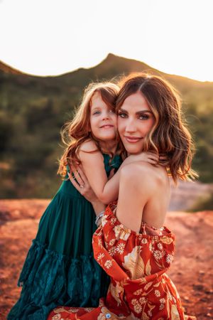 Mother and daughter in colorful dresses embrace during sunset in desert landscape.