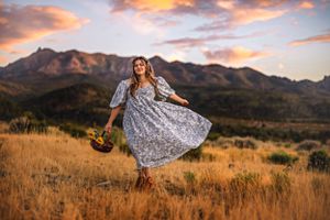 A woman in a floral dress twirls in a mountain meadow at sunset near Pine Valley Utah, Southern Utah