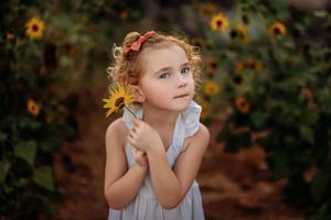 Young girl in white dress poses dreamily among blooming sunflowers.