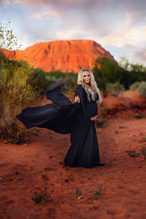 A flowing black dress contrasts against red rock formations during a dramatic sunset photo session in Southern Utah