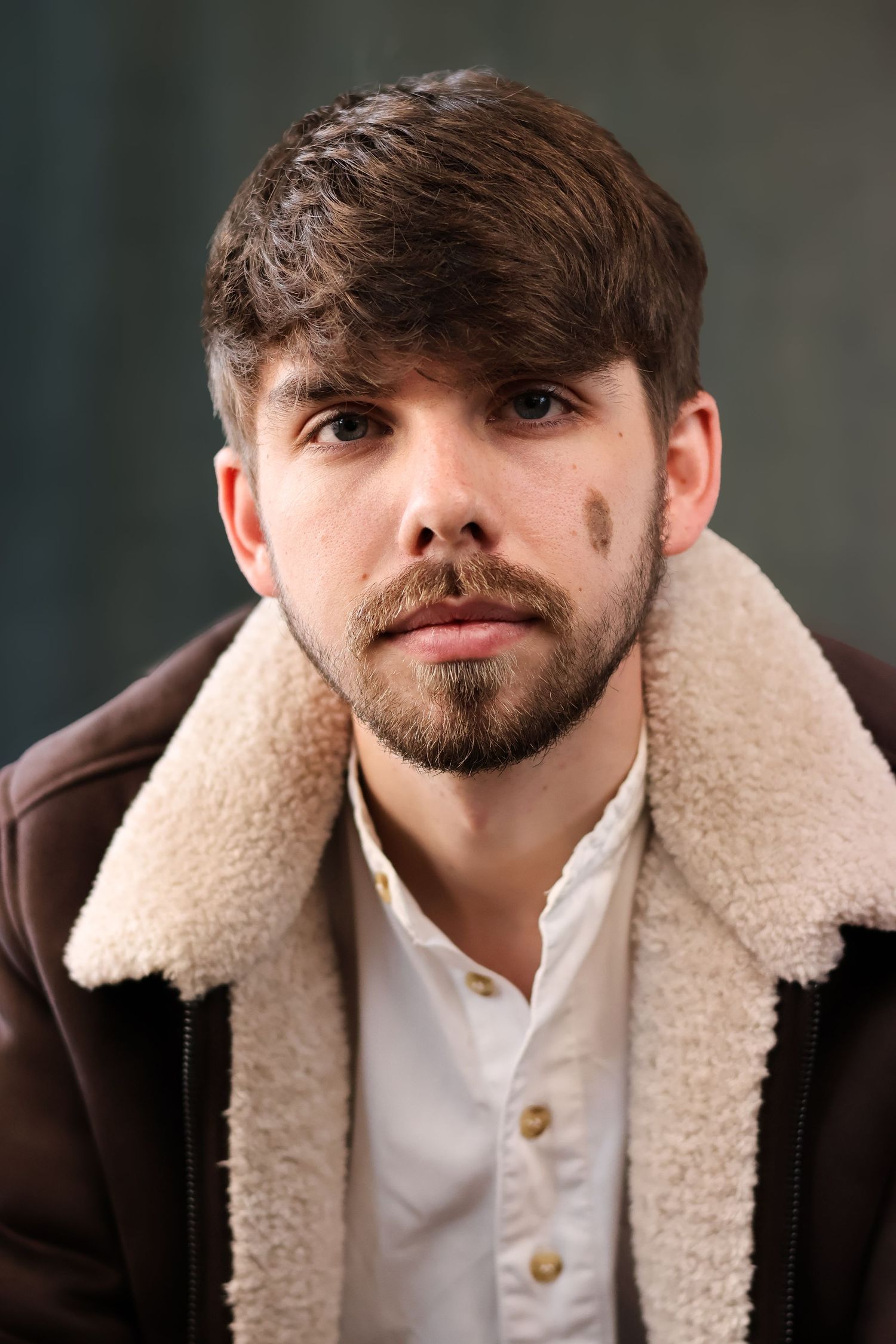 Portrait of person with beard wearing shearling collar jacket and white button-up shirt.