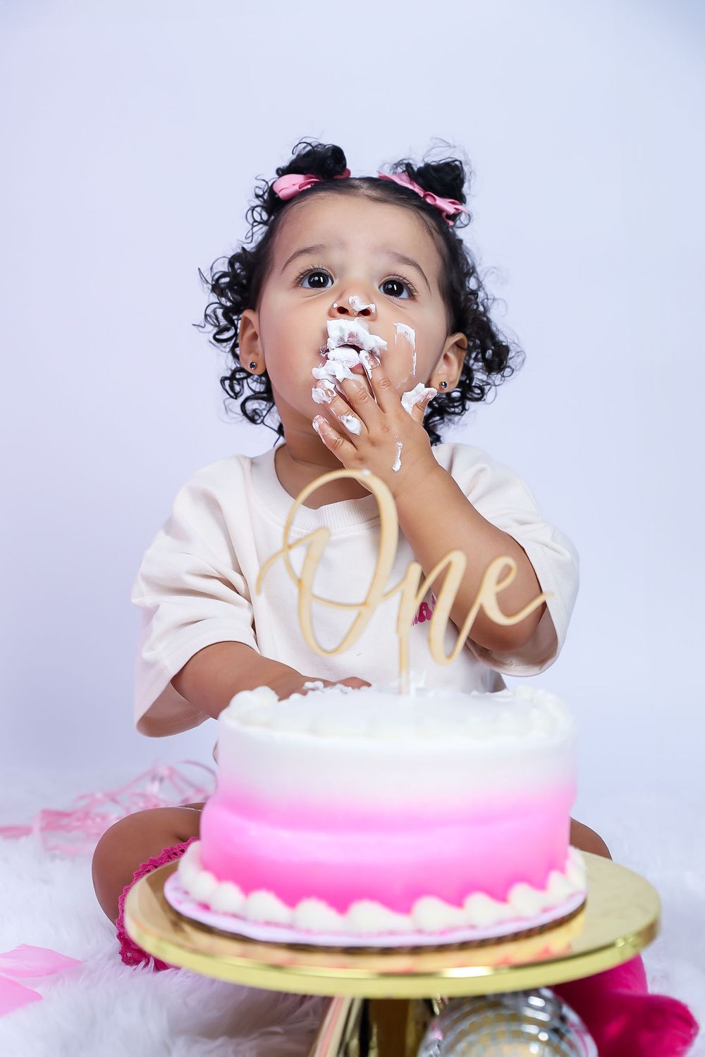 A toddler with frosting on face enjoys their first birthday cake smash.