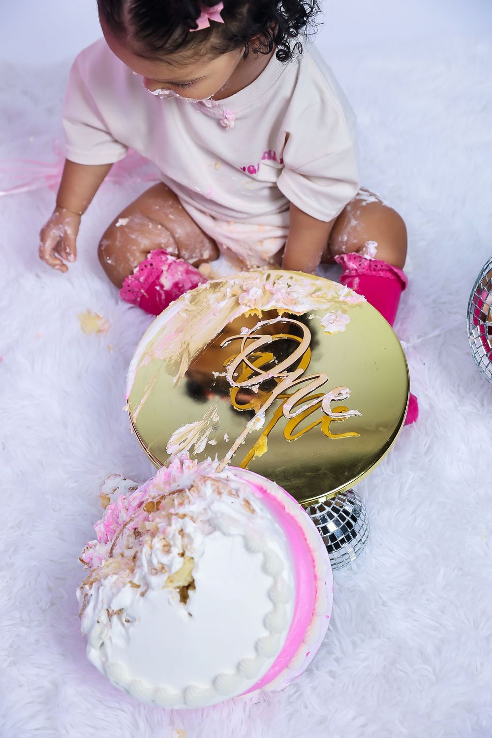 An overhead view of a smashed cake with gold decor and pink frosting during a cake smash photoshoot.