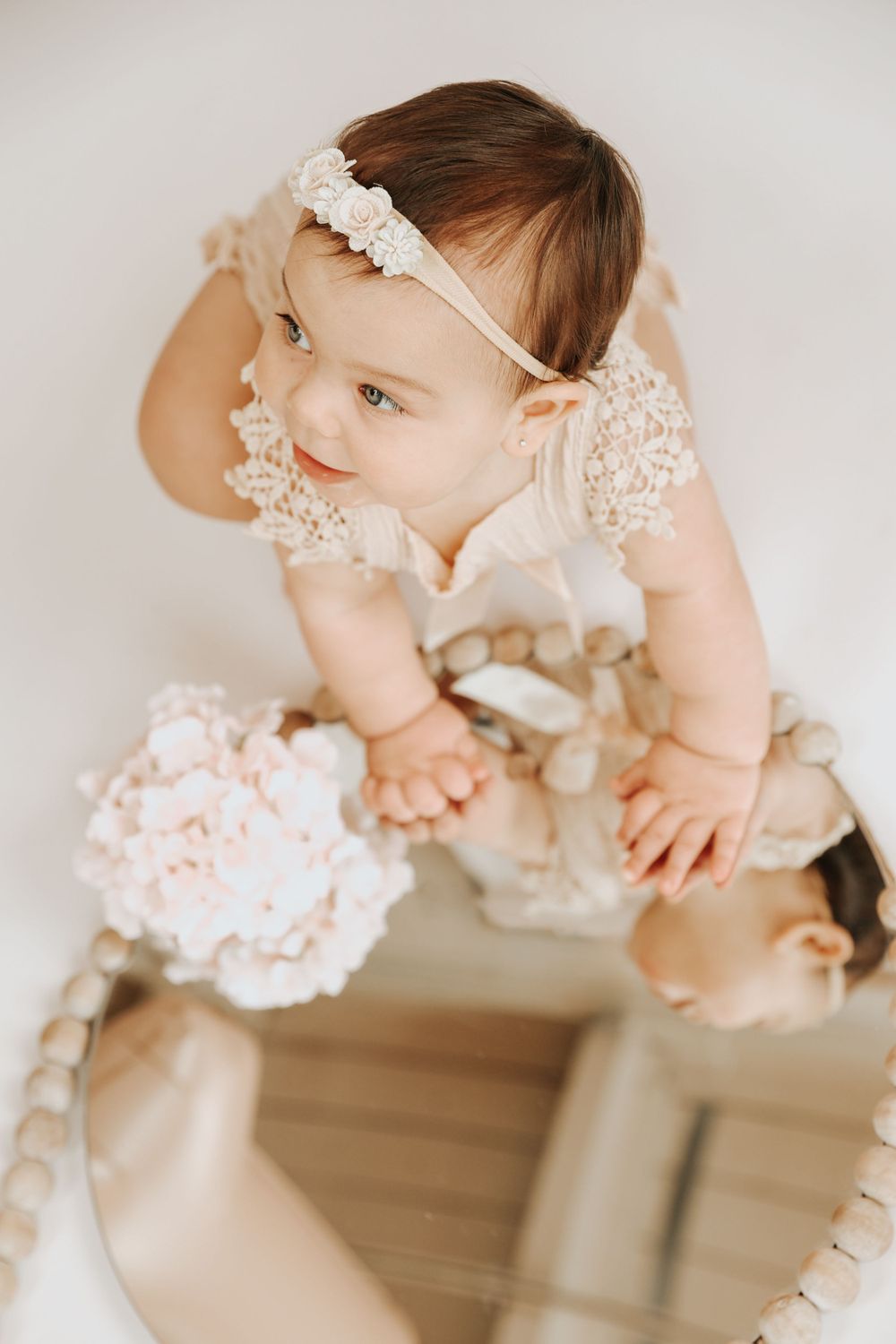 Baby in delicate lace dress poses for milestone photos on white background.