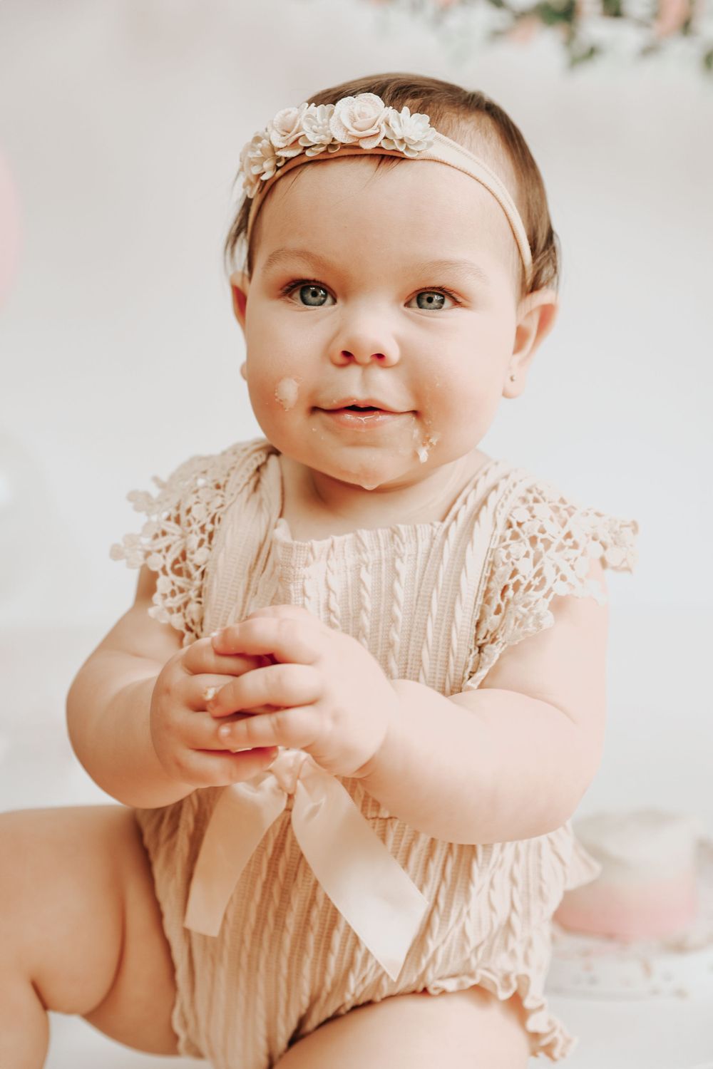Baby wearing vintage-style lace outfit smiles during portrait session against white background.
