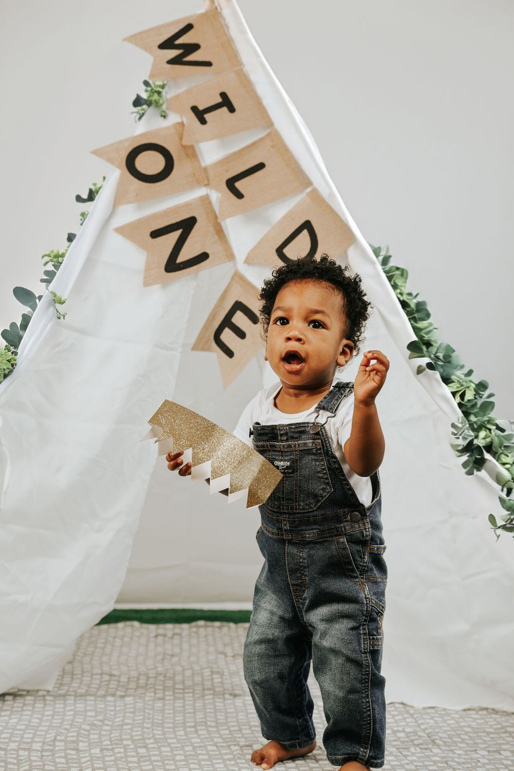 Toddler playing and standing by white teepee tent with letter banner decorations.