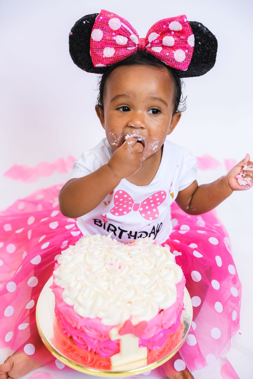 A toddler in Minnie Mouse ears and polka dot dress enjoys birthday cake.