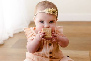 A baby in a pink dress sits on a wooden floor playing with a stuffed toy.