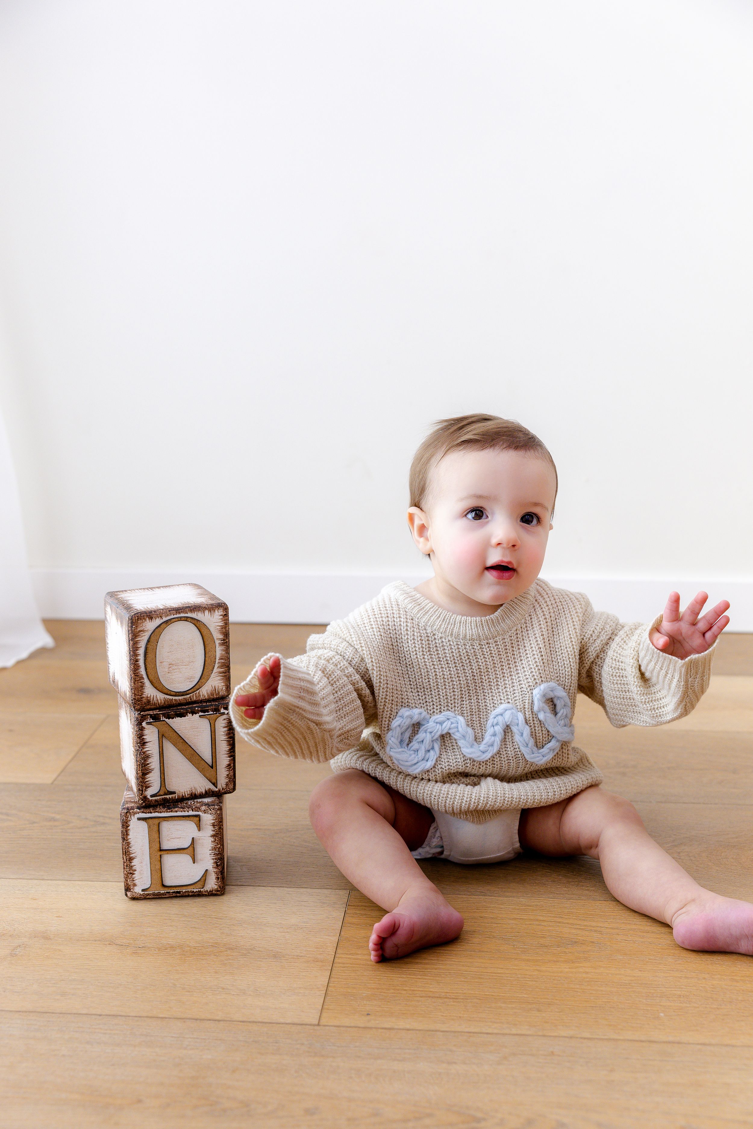 Baby in cream sweater crawls on wooden floor while playing with wooden blocks.