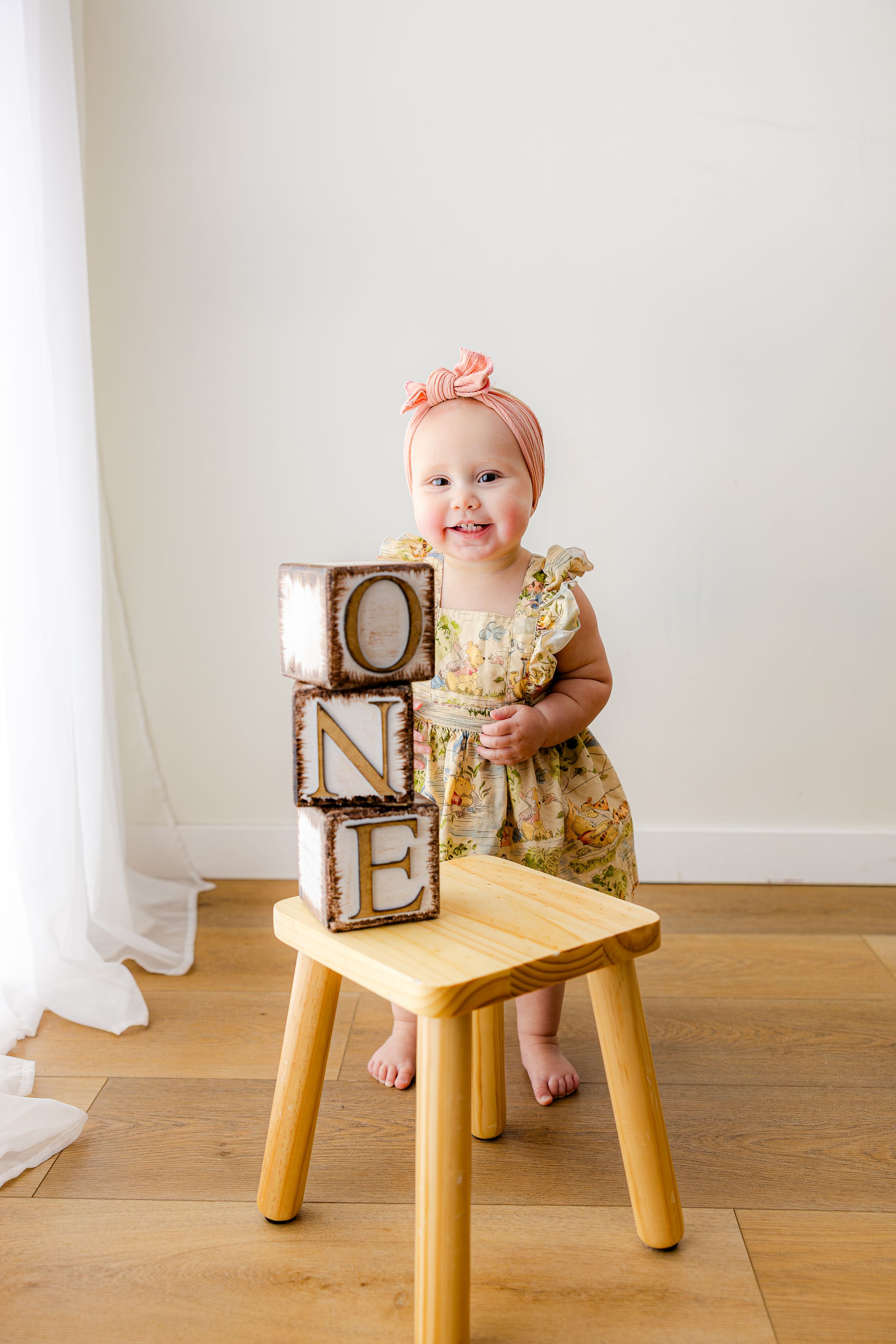 Three sequential photos show a small child sitting on a wooden stool against a white wall wearing a floral dress.
