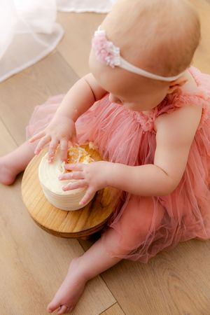 Baby in pink tulle dress smashes cake on wooden floor during first birthday photoshoot.