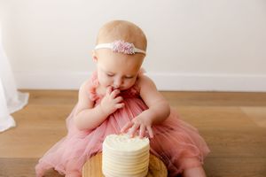 Baby in pink tulle dress sits on wooden floor during first birthday cake smash photo session.