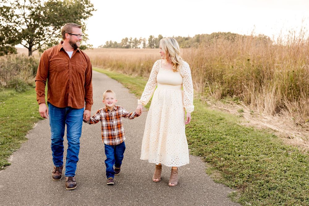Family walks together on a country path surrounded by autumn grasses and golden light at sunset.