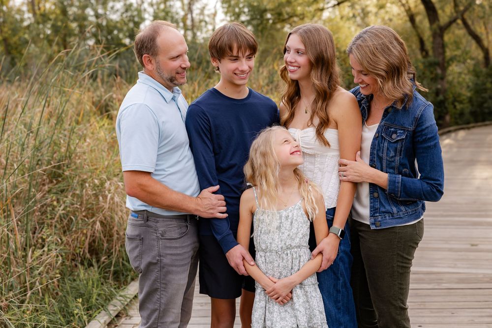 A family shares joyful moments together while walking on a wooden boardwalk during a golden sunset photo session.