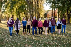 A group of people standing together outdoors on fallen autumn leaves with trees in golden sunlight.