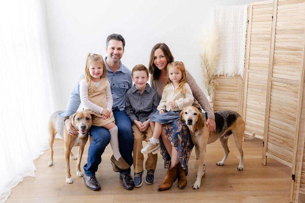 A family sits on wooden steps with their golden retriever dogs in a casual indoor photo session.
