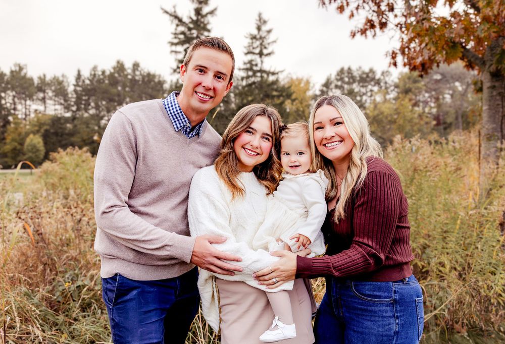 A family wearing coordinated fall outfits poses together in a golden autumn field during sunset.
