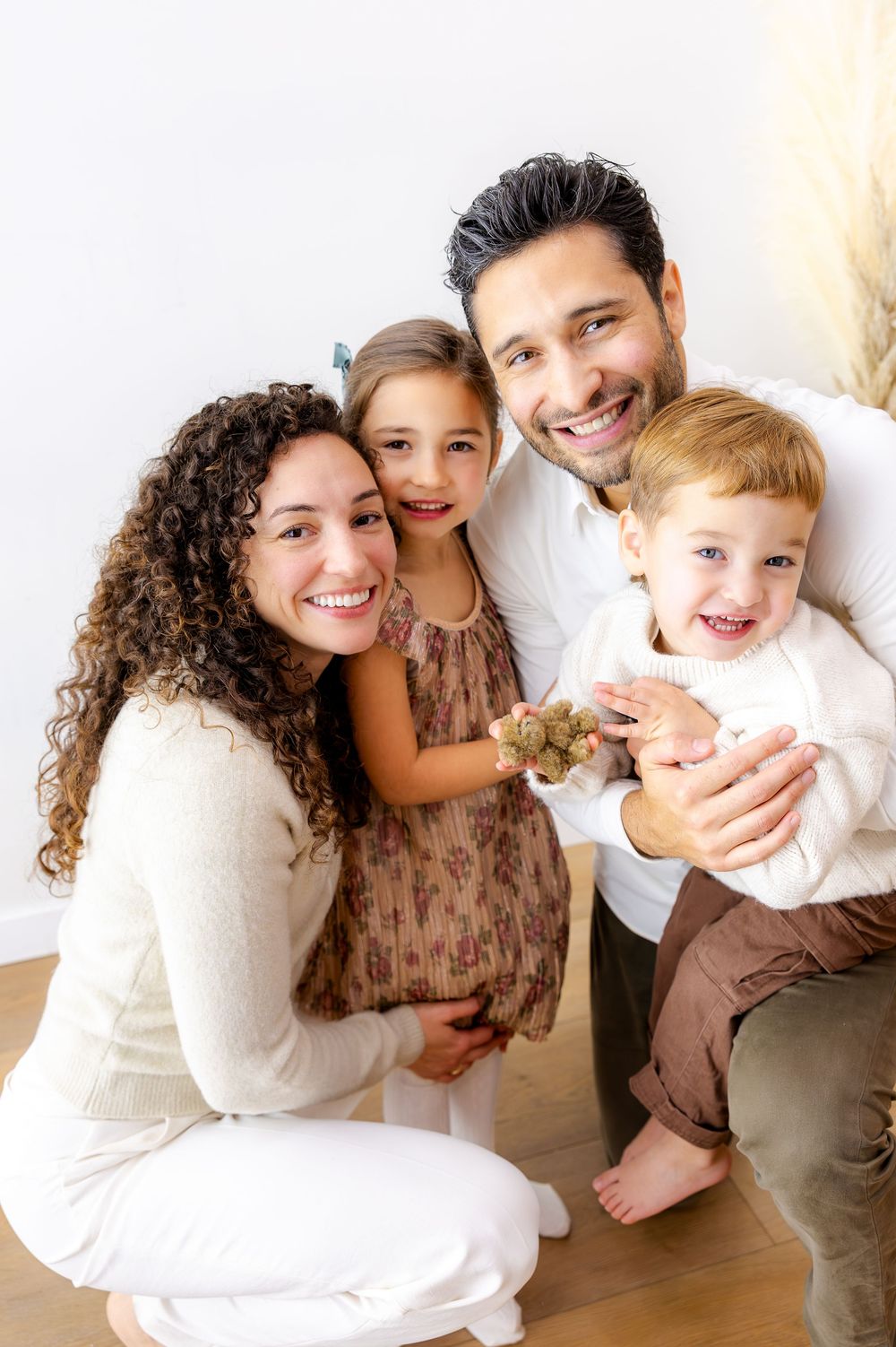 A happy family of four poses together indoors wearing coordinated neutral-toned outfits.