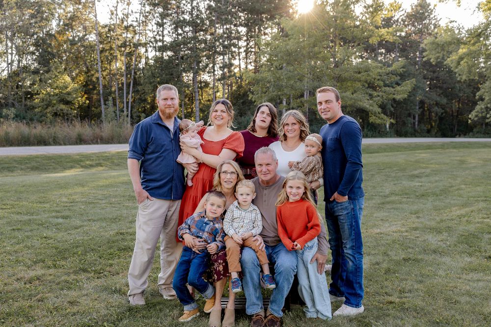 A group poses together outdoors during golden hour in coordinated blue and orange outfits for a family photo session.
