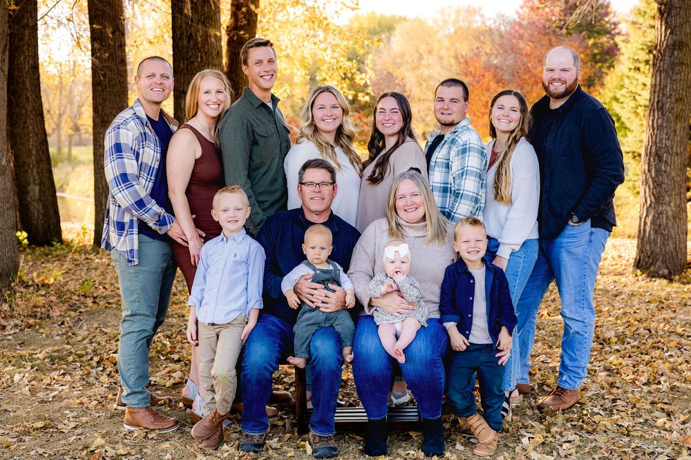 A large family group poses together outdoors among autumn trees with golden yellow leaves in the background.