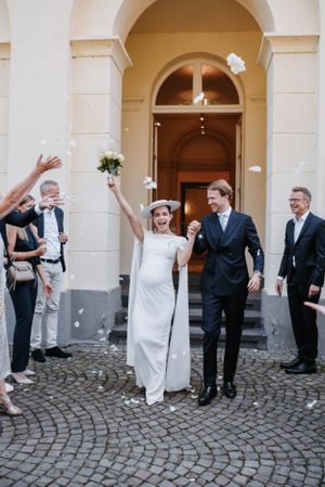 Wedding celebration outside historic building with guests tossing flower petals at the newlyweds.