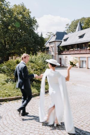 Couple strolls along cobblestone path near historic building during wedding photoshoot.