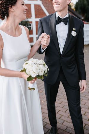 A joyful couple holding hands at their wedding, with bride in classic white dress and groom in black tuxedo with bowtie.