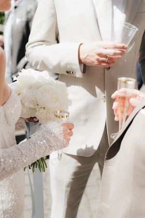 Close-up view of wedding rings and white bouquet held against light-colored formal attire.