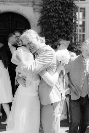 People in white dresses and formal attire laugh together in a candid line-up photo during an outdoor event.