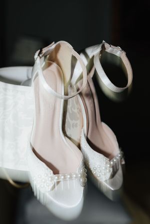 Elegant white bridal shoes with pearl embellishments and ankle straps on a light background.