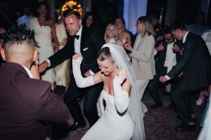 A joyful bride in a white wedding dress dances energetically on a crowded dance floor during a wedding reception.