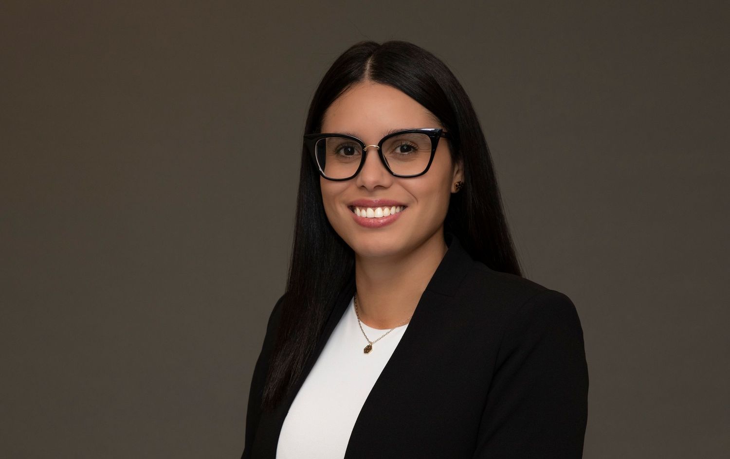 Professional headshot of a person in glasses wearing a black blazer against a dark background.