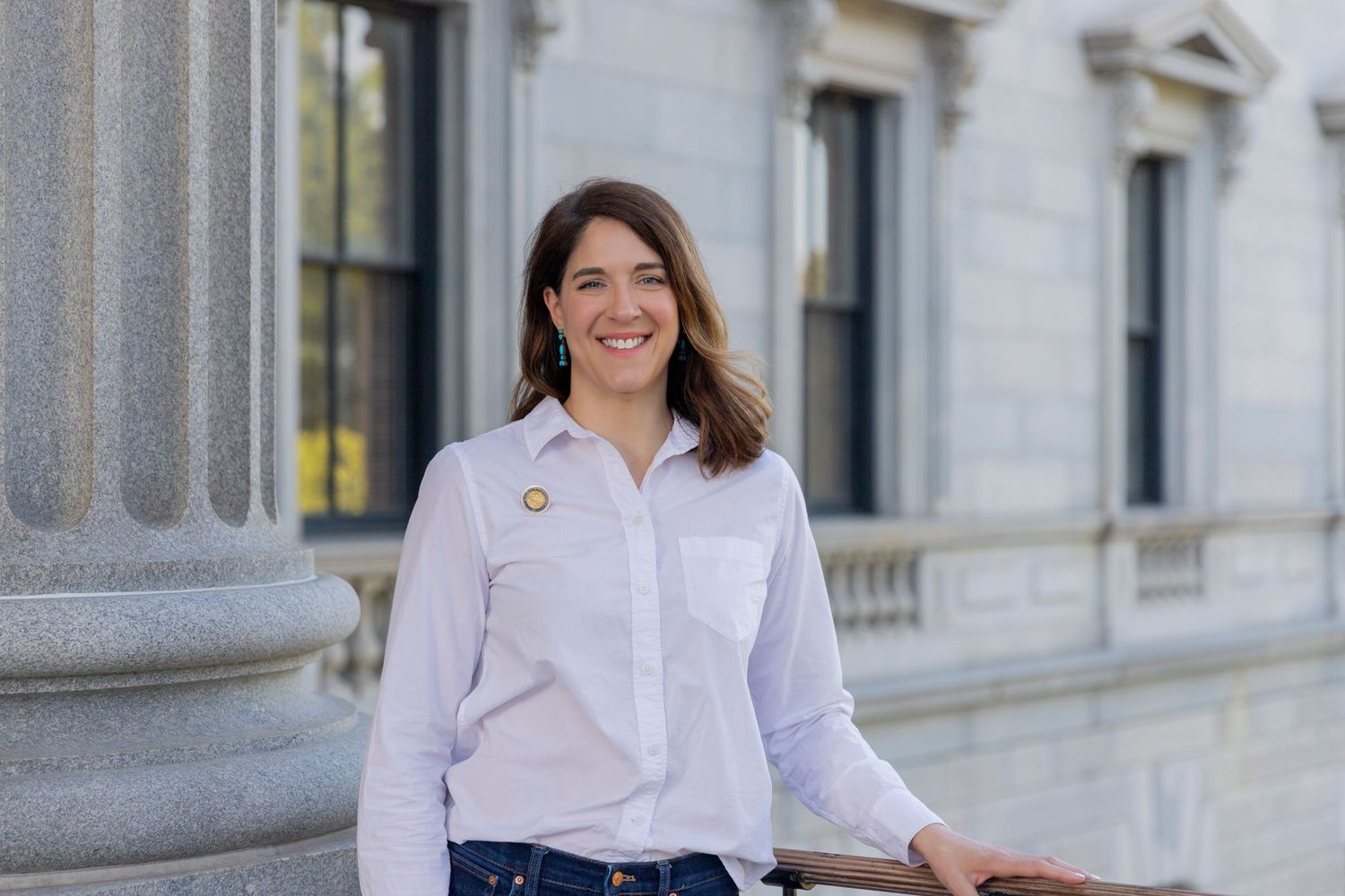 Professional wearing a white button-down shirt stands smiling near a stone column building exterior.