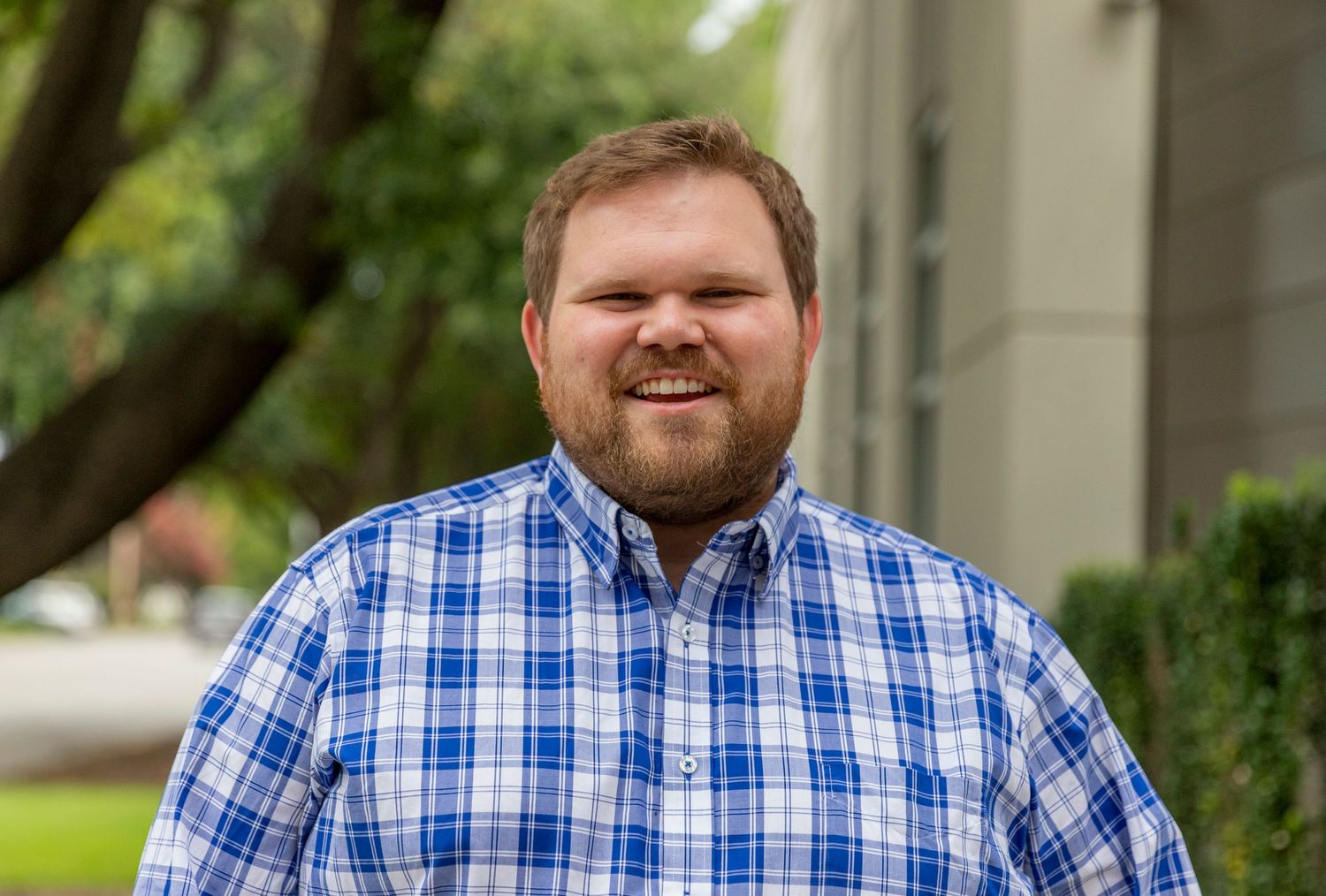 Outdoor portrait of person in blue plaid button-down shirt smiling at camera.