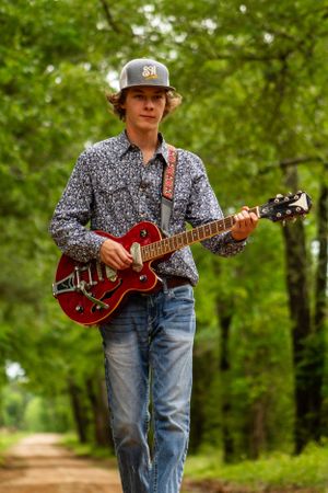 Casual outdoor photoshoot with someone playing a red electric guitar in nature.