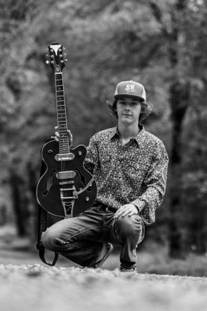 Black and white portrait with acoustic guitar and baseball cap in outdoor autumn setting.