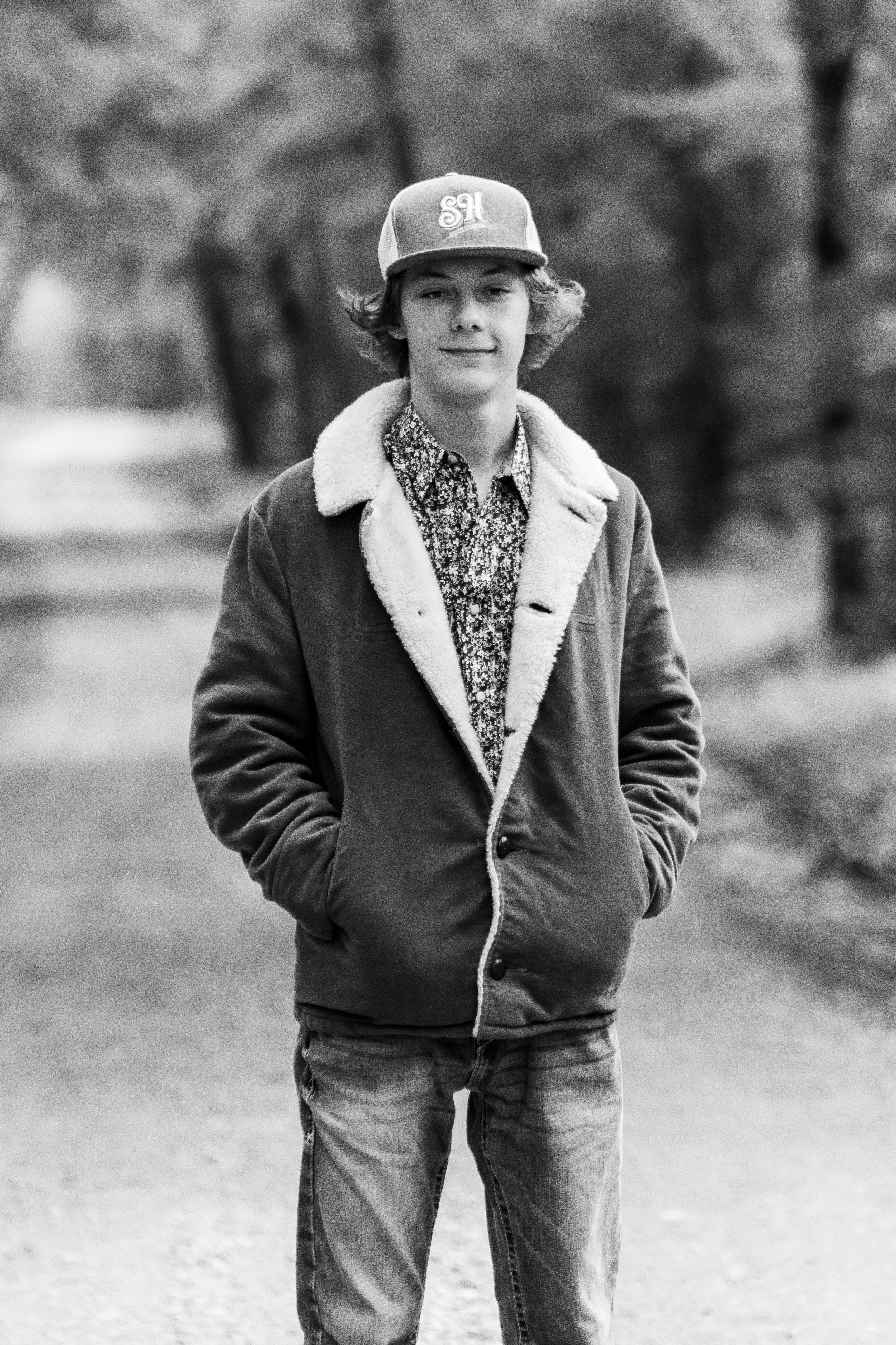 Person in winter jacket and baseball cap walking outdoors in black and white photo.