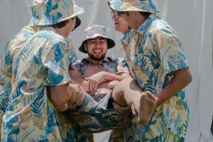 Group wearing coordinated Hawaiian shirts laugh and pose together at an outdoor event.