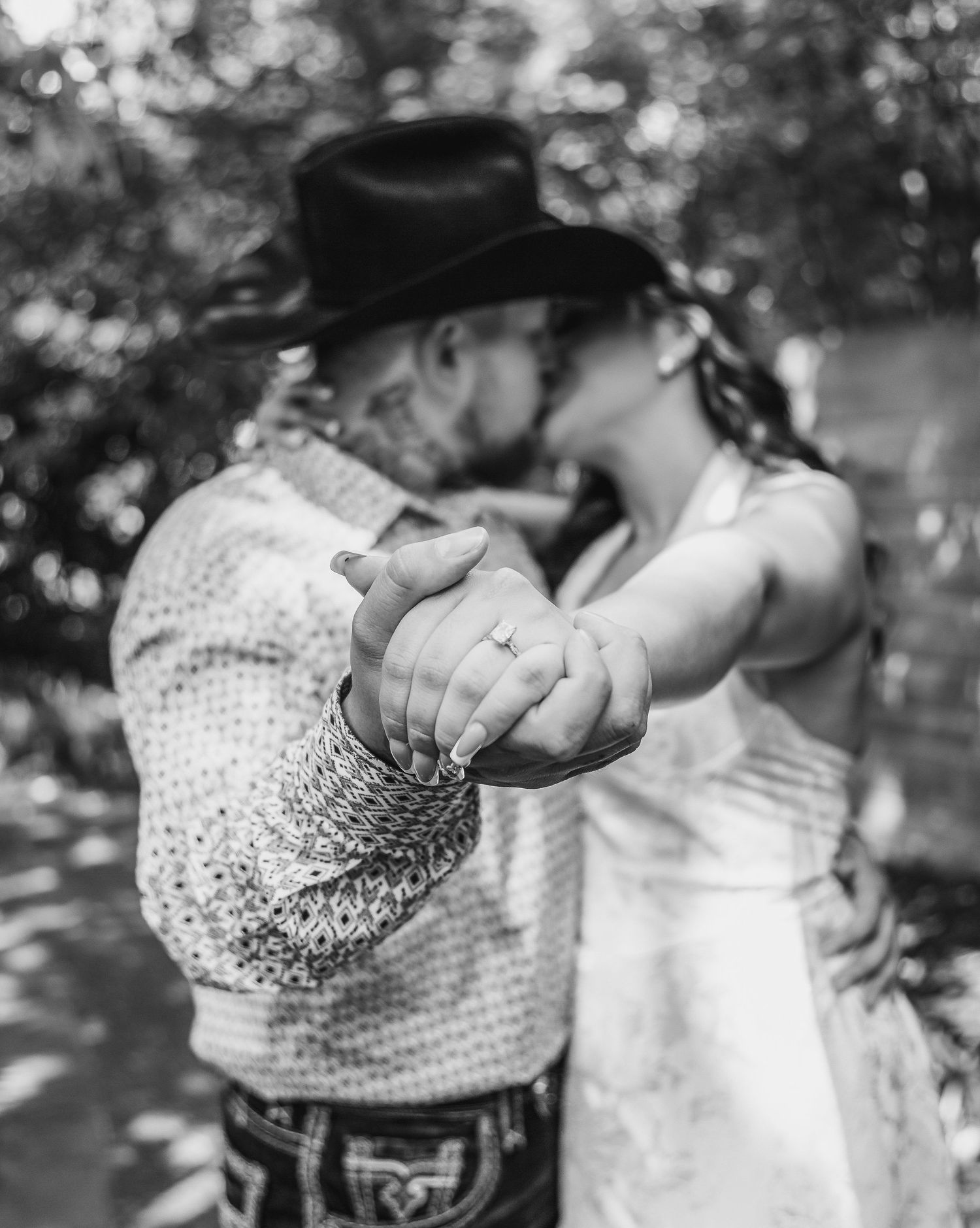 Black and white portrait of parents sharing intimate moment with baby in forest setting.