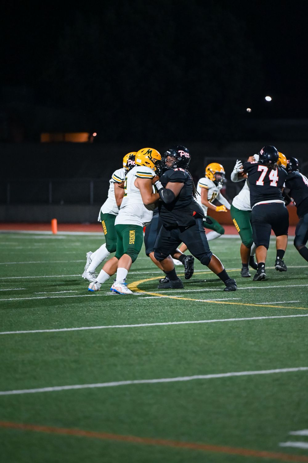 Football players from two teams clash at the line of scrimmage during a night game.