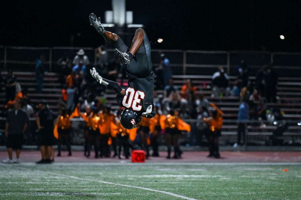 Player performs an acrobatic backflip on the football field at night.