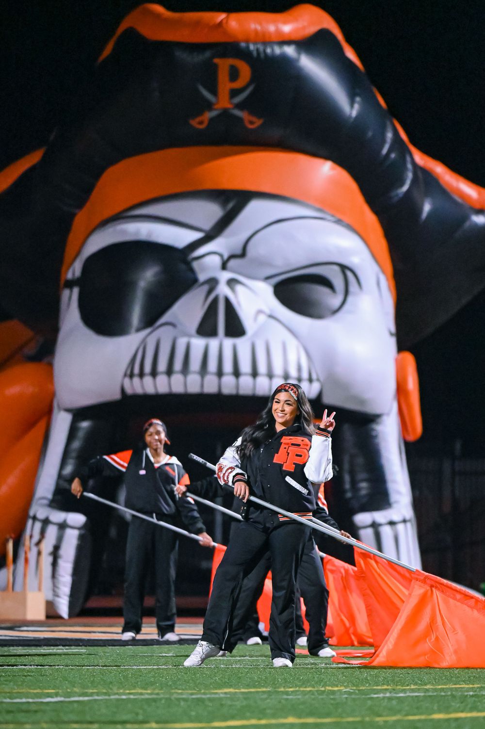 Performers dance in front of a large inflatable pirate skull mascot with orange and black colors.