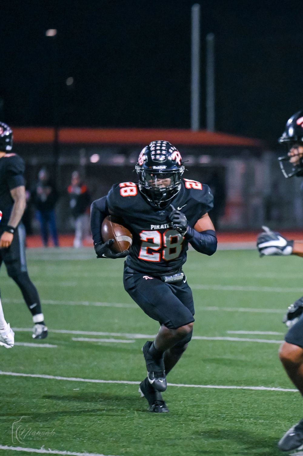 Football players in black uniforms dive and leap across the field during a game.
