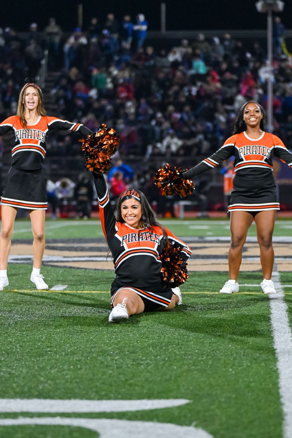 Cheerleaders in orange and black uniforms perform a synchronized routine on the football field.