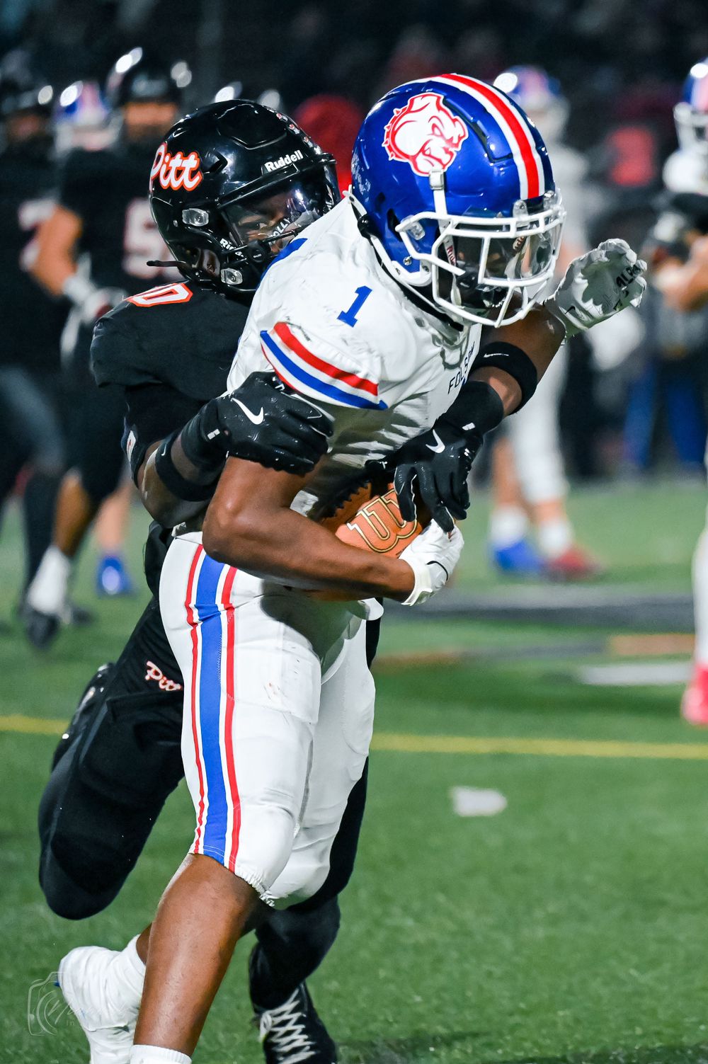 Football players tackle an opponent in white and blue uniform during an intense game moment.