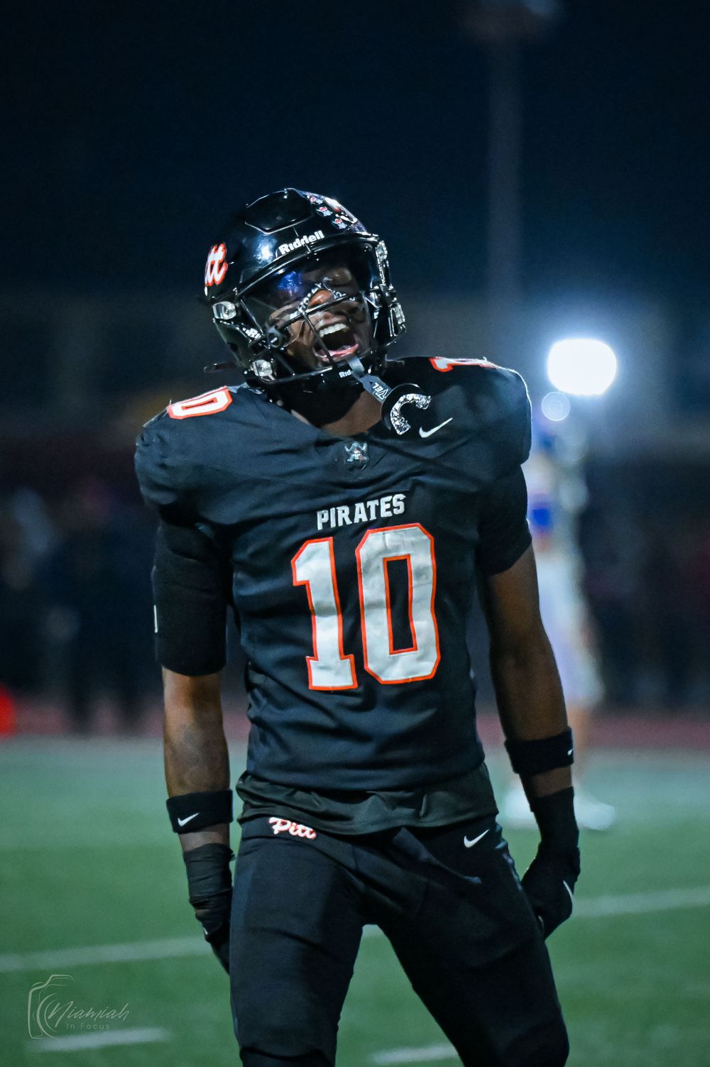 Pirates football players in black uniforms with number 10 jersey on the field at night.